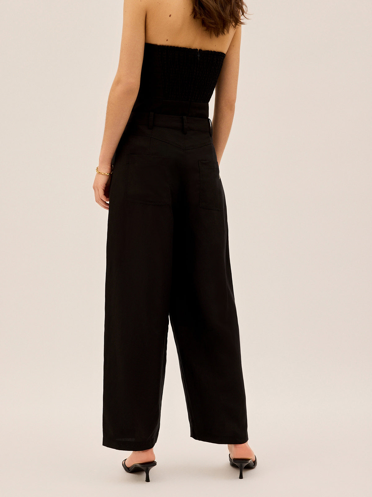 Andie Black Linen Blend Barrel Trousers by Kitri Studio. Say hello to Andie, your new go-to trousers for effortless style and modern tailoring.  Designed with a mid-rise waist and a barrel-leg silhouette, these trousers offer a relaxed yet structured fit that feels as good as it looks. Button and zip fly front. Slanted pockets. Loose fit. Shell: 80%% Lenzing Tencel™ Lyocell 20%% Linen Lining: 100%% Recycled Polyester.