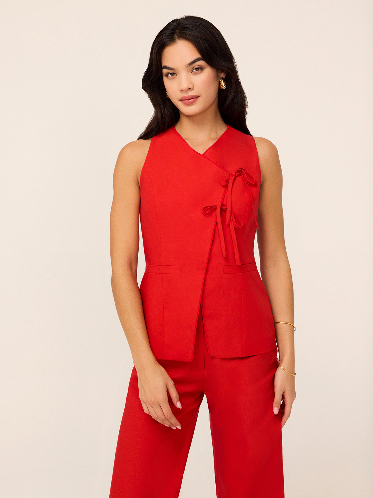Lea Red Tie Front Waistcoat by Kitri Studio. Step into effortless sophistication with our Lea waistcoat - a contemporary take on classic tailoring that adds instant polish to any look.  This vibrant red piece features a thoughtfully designed signature tie detail at the front that creates a flattering and elegant asymmetric finish while adding a touch of playful twist. V-neck. Sleeveless. Front ties. SHELL: Lenzing TM 70%% Tencel 30%% Linen Lining: 100%% Recycled Polyester.