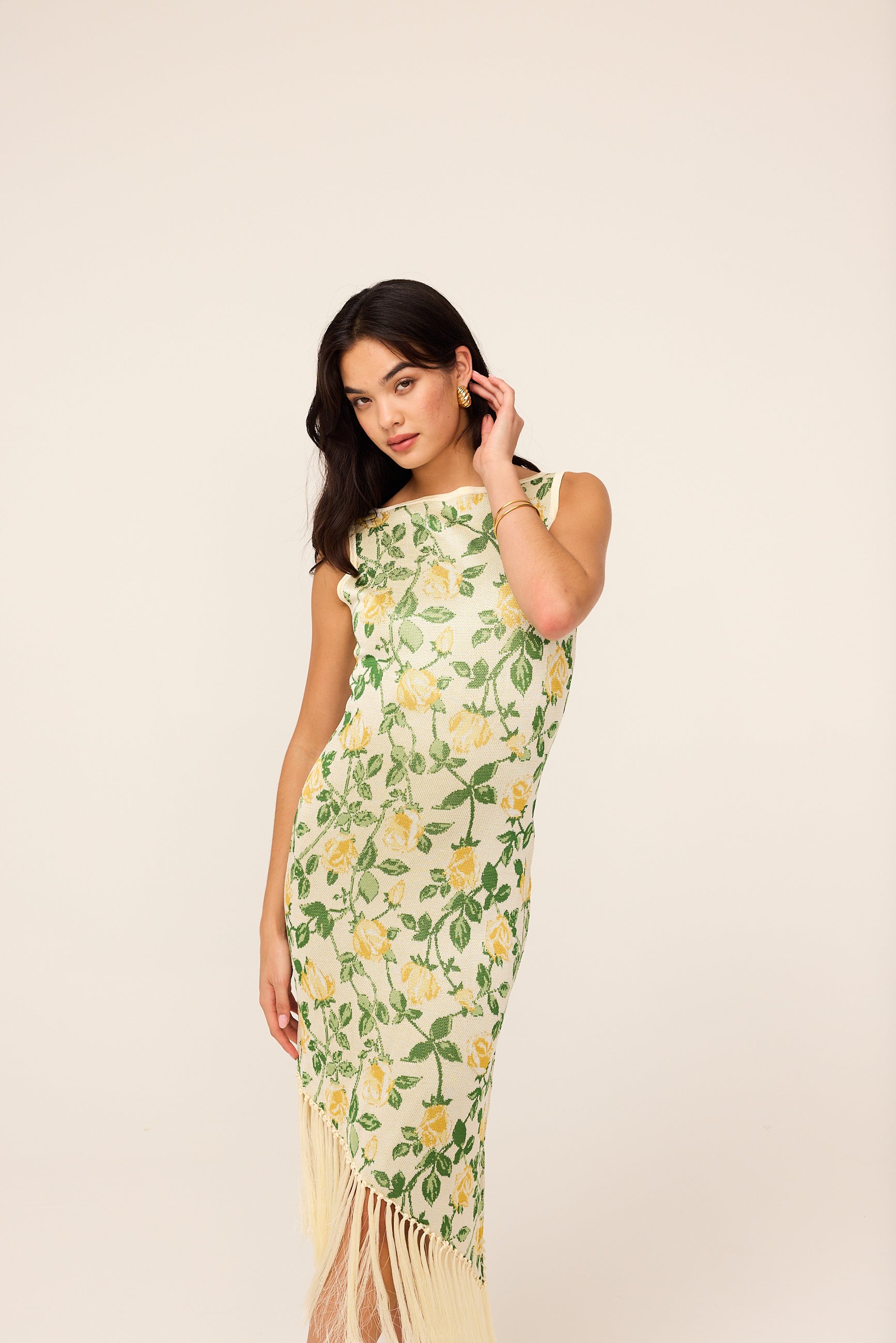 Tabara Yellow Rose Knit Dress by Kitri Studio. A statement dress with a nostalgic twist.  The Tabara Dress is a midi knitted masterpiece, featuring an all-over yellow rose jacquard motif and a striking asymmetric hemline with fringe detailing—because who doesn’t love a little movement? The wide ‘90s-inspired neckline gives it a modern yet retro feel, while the figure-hugging fit ensures maximum impact. Slash Neck. Sleeveless. Delicate. 60%% Cotton 40%% Viscose.