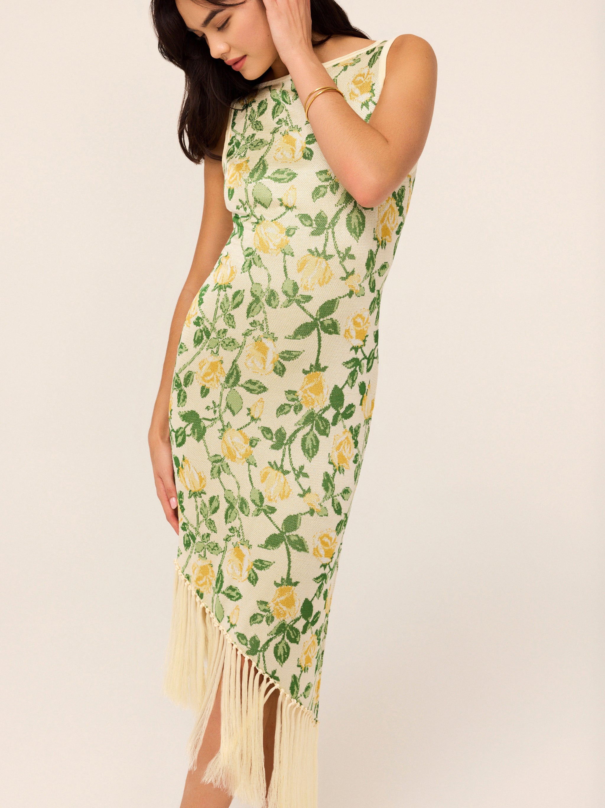 Tabara Yellow Rose Knit Dress by Kitri Studio. A statement dress with a nostalgic twist.  The Tabara Dress is a midi knitted masterpiece, featuring an all-over yellow rose jacquard motif and a striking asymmetric hemline with fringe detailing—because who doesn’t love a little movement? The wide ‘90s-inspired neckline gives it a modern yet retro feel, while the figure-hugging fit ensures maximum impact. Slash Neck. Sleeveless. Delicate. 60%% Cotton 40%% Viscose.