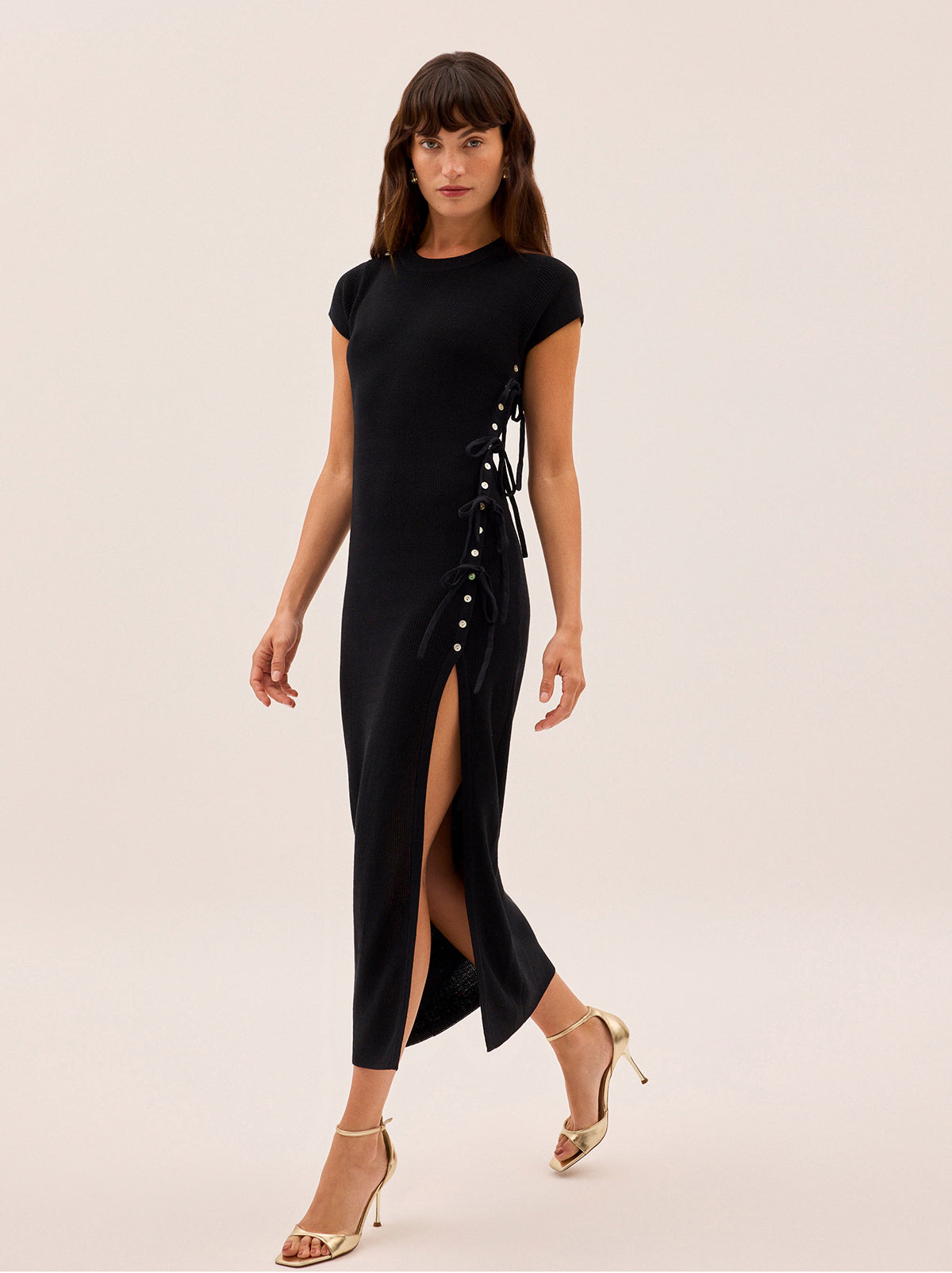 Calista Black Knit Dress by Kitri Studio. Introducing the Calista dress, our striking new silhouette in a soft yet structured cotton-nylon knit.  Designed with a classic round neckline and a body-skimming fit, it features an asymmetric front button closure with adjustable tie details and a dramatic thigh-high split. Round neck. Cap sleeves. Button front. 68% Cotton, 32% Nylon.