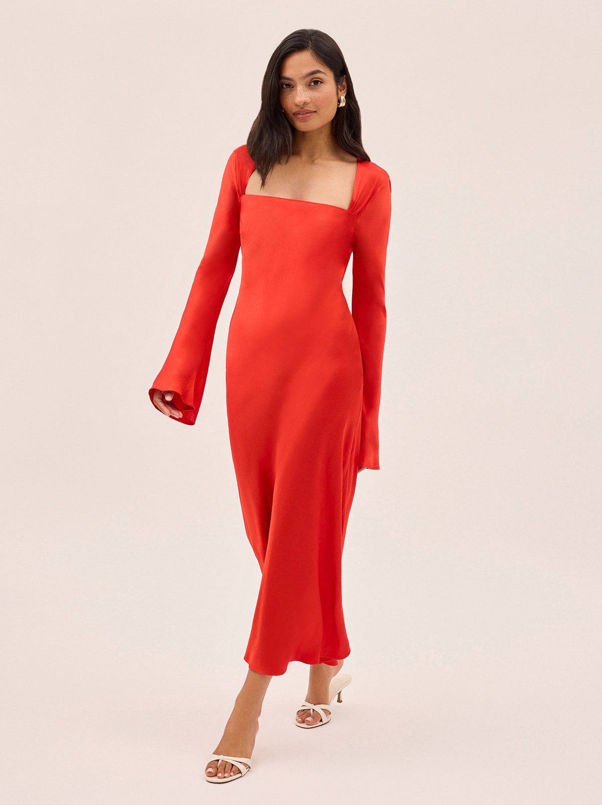 Camille Red Satin Dress by Kitri Studio. Cut on the bias for a fluid, body-skimming fit, the Camille dress is crafted from lustrous viscose satin in a vibrant, head-turning red.  The square neckline adds a touch of elegance, while long, flared sleeves add a touch of drama and movement. Square neckline. Flared sleeves. Concealed side-zip. 100% Viscose Satin.