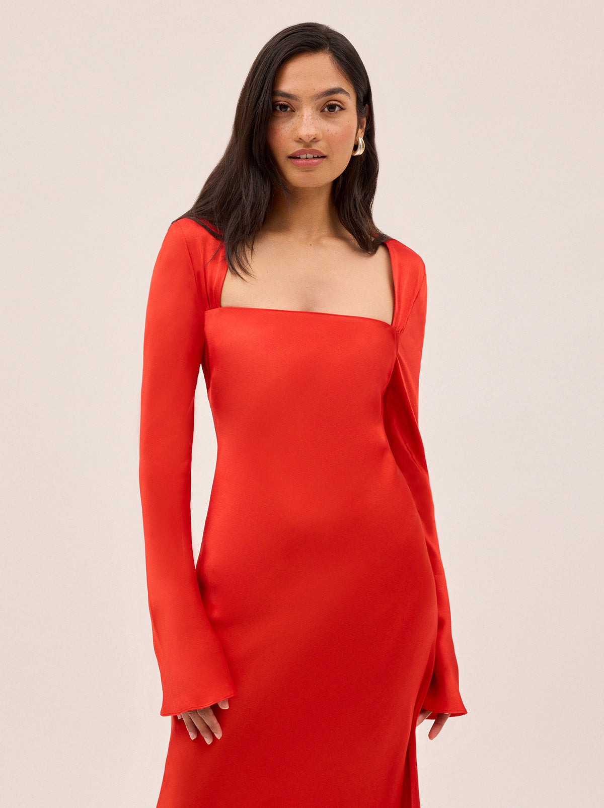 Camille Red Satin Dress by Kitri Studio. Cut on the bias for a fluid, body-skimming fit, the Camille dress is crafted from lustrous viscose satin in a vibrant, head-turning red.  The square neckline adds a touch of elegance, while long, flared sleeves add a touch of drama and movement. Square neckline. Flared sleeves. Concealed side-zip. 100% Viscose Satin.