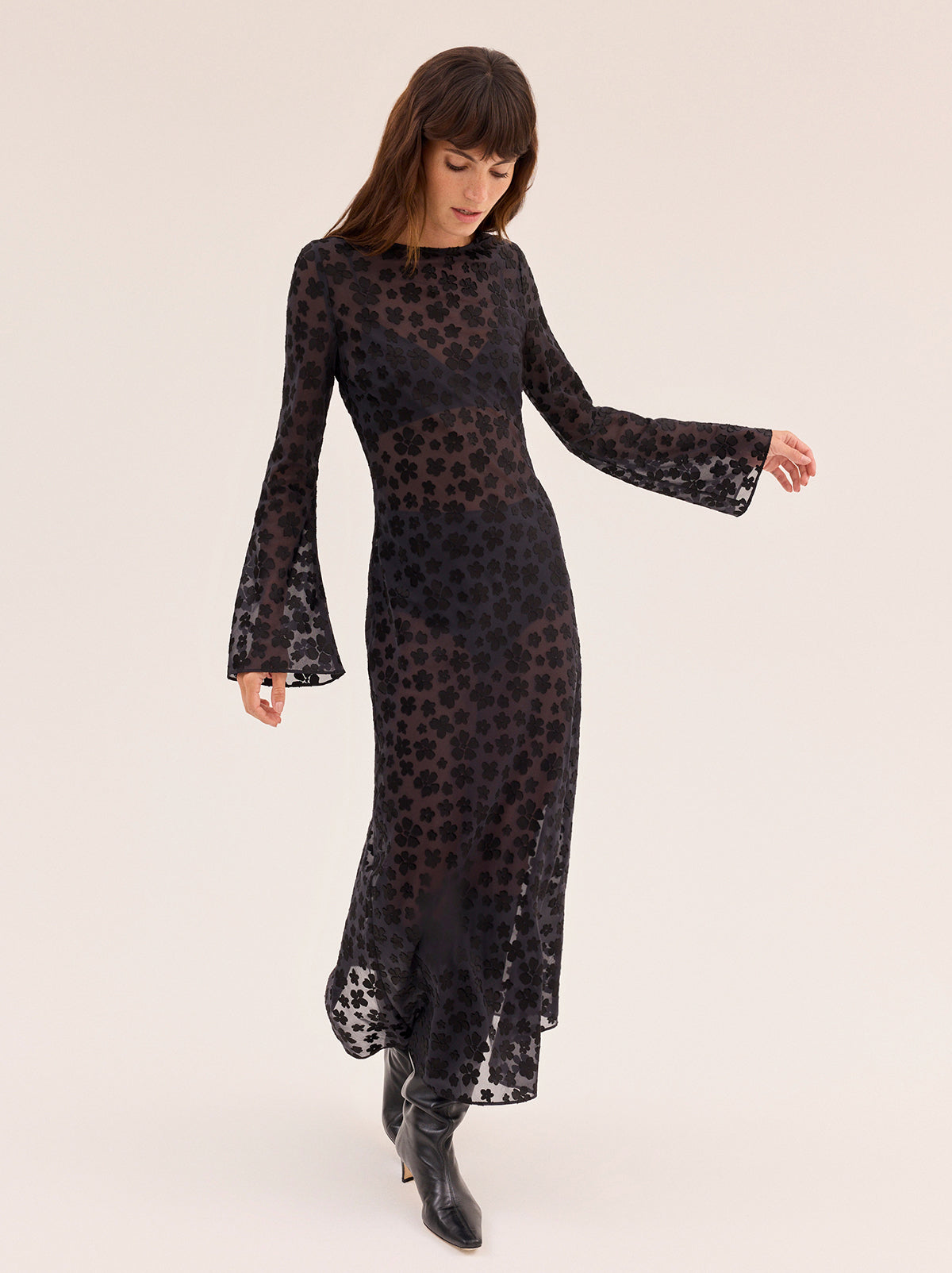 Giselle Black Floral Dress by Kitri Studio. Giselle Black Floral Dress is cut from semi-sheer satin burnout in an in-house designed black floral pattern that brings subtle texture and depth.  The bias-cut silhouette skims the body before flowing into a fluid midi length, while long flared sleeves and a wide boatneck create an elegant balance of ease and drama. Slash Neck. Long sleeves. Sheer. 75% Viscose, 25% Nylon.