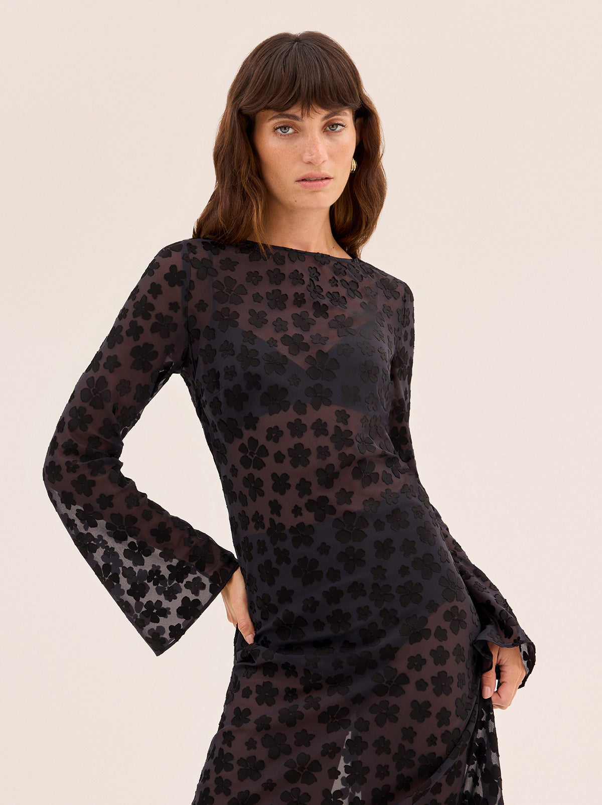 Giselle Black Floral Dress by Kitri Studio. Giselle Black Floral Dress is cut from semi-sheer satin burnout in an in-house designed black floral pattern that brings subtle texture and depth.  The bias-cut silhouette skims the body before flowing into a fluid midi length, while long flared sleeves and a wide boatneck create an elegant balance of ease and drama. Slash Neck. Long sleeves. Sheer. 75% Viscose, 25% Nylon.