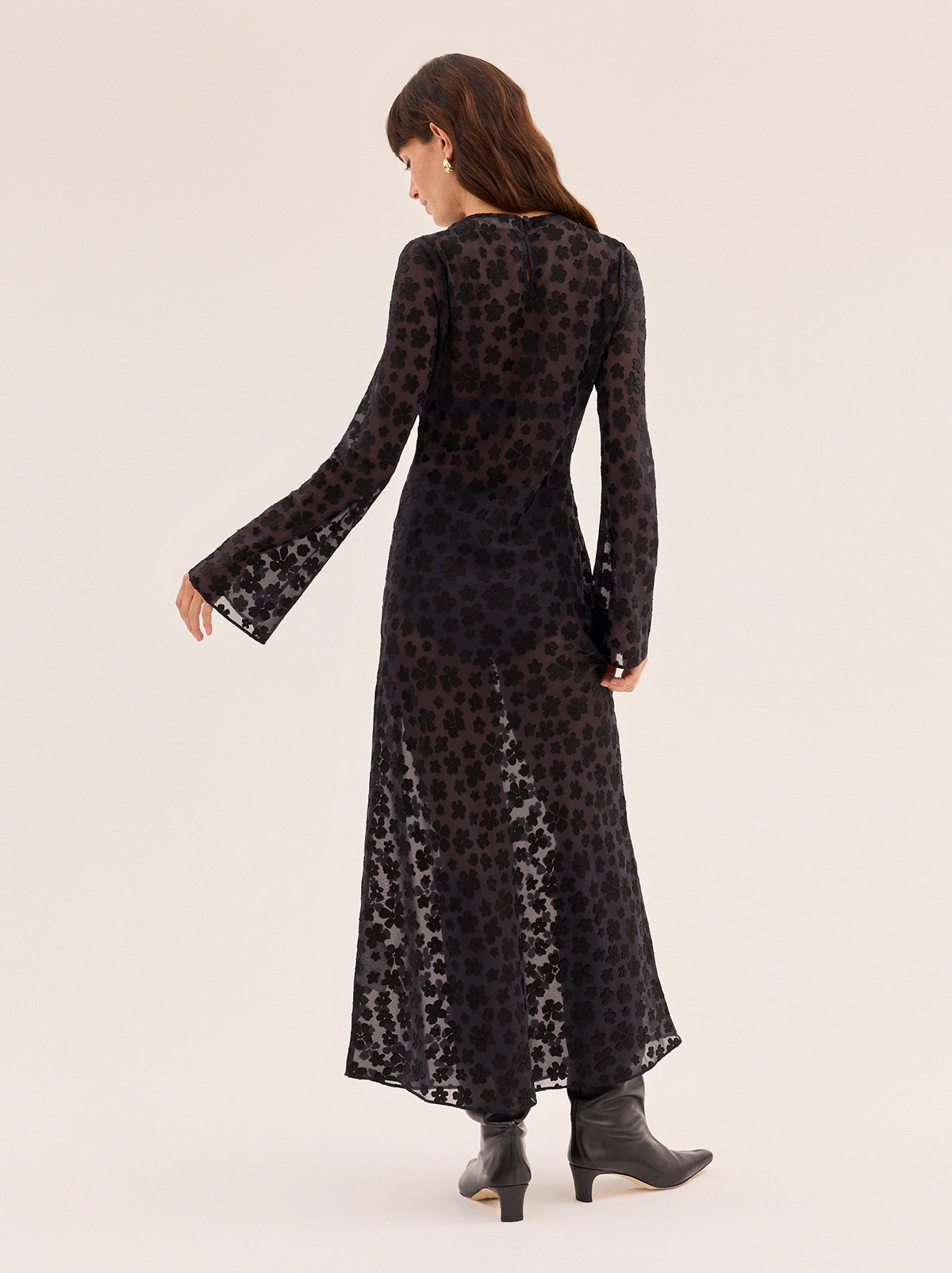 Giselle Black Floral Dress by Kitri Studio. Giselle Black Floral Dress is cut from semi-sheer satin burnout in an in-house designed black floral pattern that brings subtle texture and depth.  The bias-cut silhouette skims the body before flowing into a fluid midi length, while long flared sleeves and a wide boatneck create an elegant balance of ease and drama. Slash Neck. Long sleeves. Sheer. 75% Viscose, 25% Nylon.