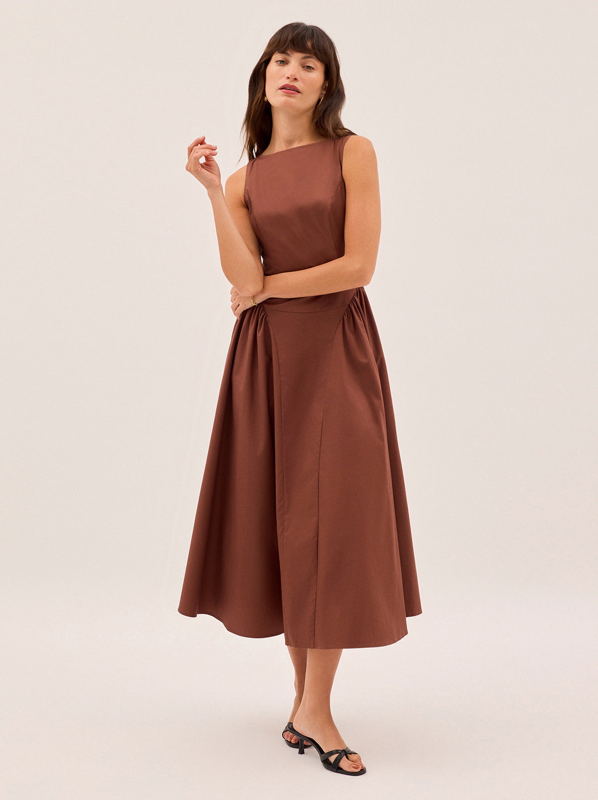 Josephine Sienna Cotton Dress by Kitri Studio. Elegant and effortless, the Josephine dress is crafted from crisp cotton in a warm sienna hue.  Featuring a flattering boat neckline and sleeveless silhouette, it’s designed with softly gathered side panels and a voluminous A-line skirt for graceful movement. Wider crew neck. Sleeveless. Centre-back zip closure. 100% Cotton.