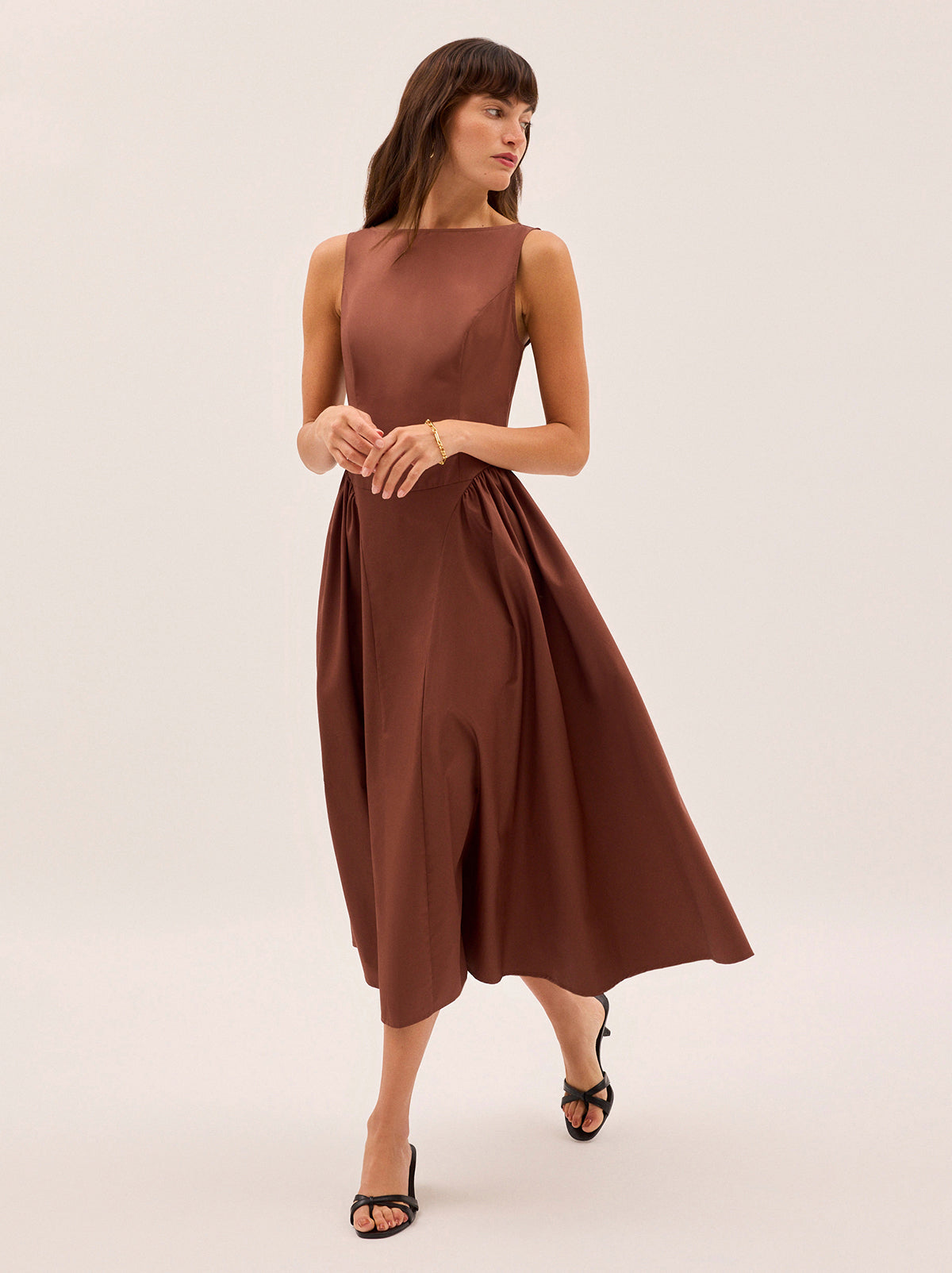 Josephine Sienna Cotton Dress by Kitri Studio. Elegant and effortless, the Josephine dress is crafted from crisp cotton in a warm sienna hue.  Featuring a flattering boat neckline and sleeveless silhouette, it’s designed with softly gathered side panels and a voluminous A-line skirt for graceful movement. Wider crew neck. Sleeveless. Centre-back zip closure. 100% Cotton.