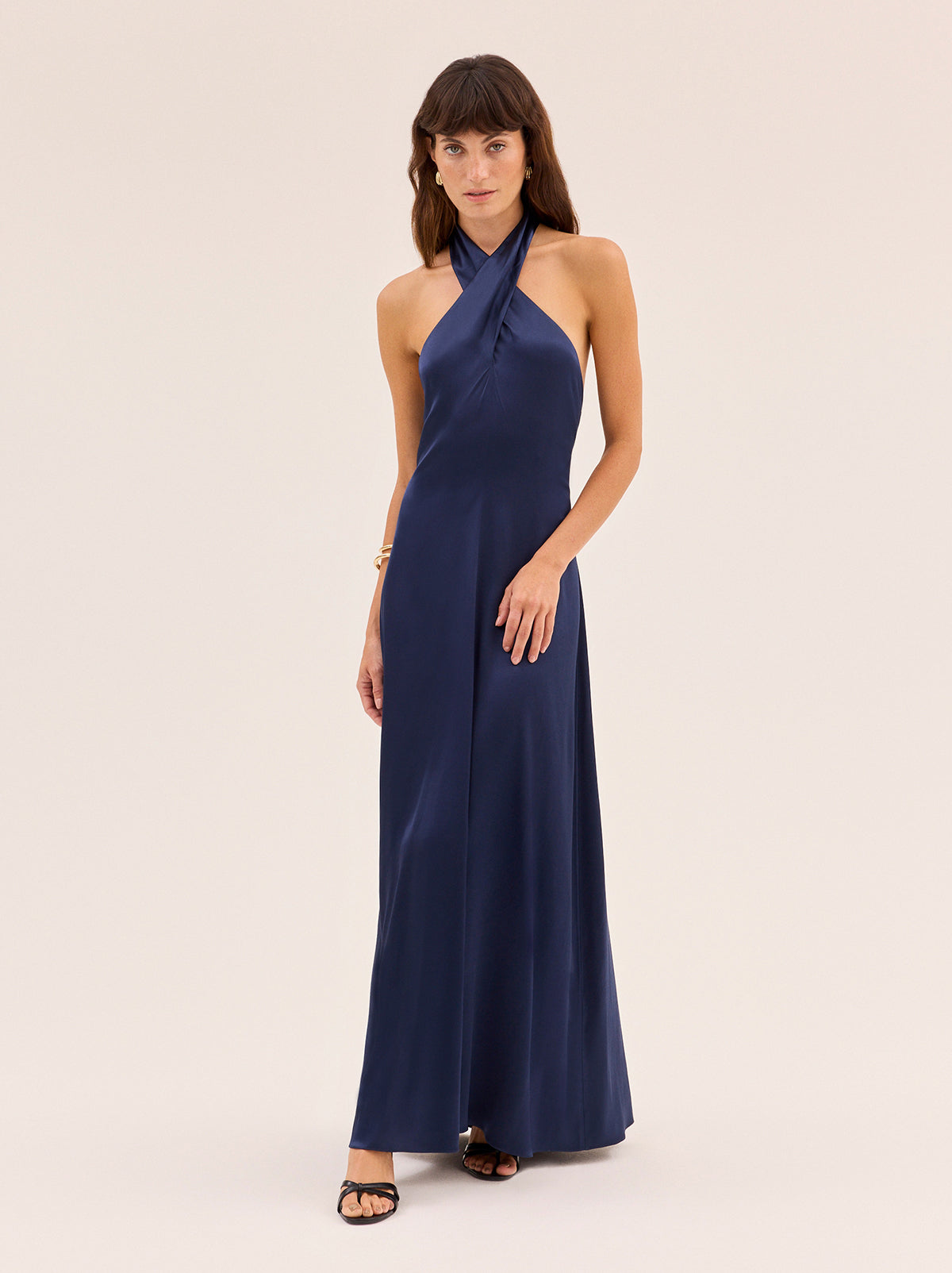 Neve Navy Satin Halterneck Dress by Kitri Studio. Neve Navy Satin Halterneck Dress is designed as a timeless wardrobe investment, combining sophistication with versatility.  Cut from fluid viscose satin, the cross-front halterneck ties at the back for a clean, elegant line, while the bias-cut skirt softly skims the body for a universally flattering fit. Halter neckline. Tie straps. Centre-back zip closure. 97% Viscose, 3% Elastane.