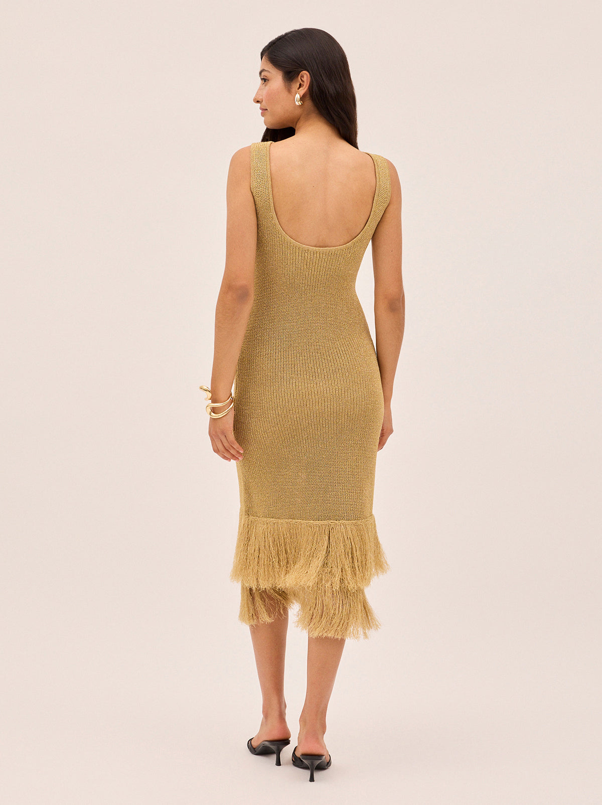 Sandra Gold Lurex Knit Dress by Kitri Studio. Sandra Gold Lurex Knit Dress in a shimmery gold lurex knit offers a body-skimming silhouette that moves effortlessly with you.  Designed with a flattering round neckline, sleeveless cut and double fringe detail at the hem, it radiates a 1920s-inspired charm, perfect for party season or any occasion that calls for a statement piece. Round neck. sleeveless. Length: Midi. 65% Viscose, 35% Lurex.