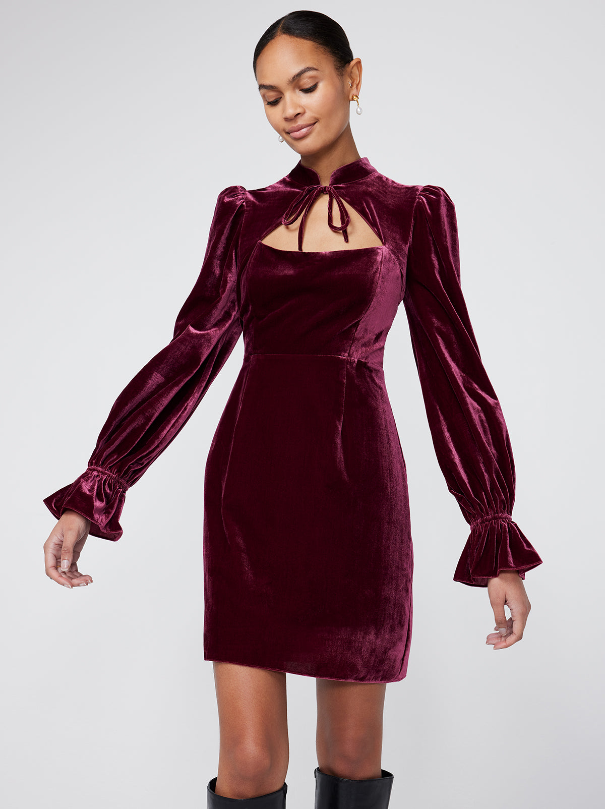 Valentina Burgundy Velvet Mini Dress By KITRI Studio is a sultry sleeved mini dress with a tie detail collar. An ideal party dress option it features puff shoulders and elasticated frilly cuffs - as well as a fitted bodice for a memorable silhouette. Deep dark red velvet fabric looks elegant and expensive.
